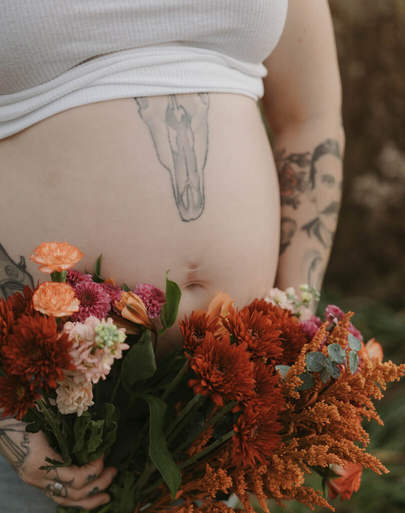 A clos-up image of a maternity session where the mother is holding a bouquet of wildflowers near her growing belly.