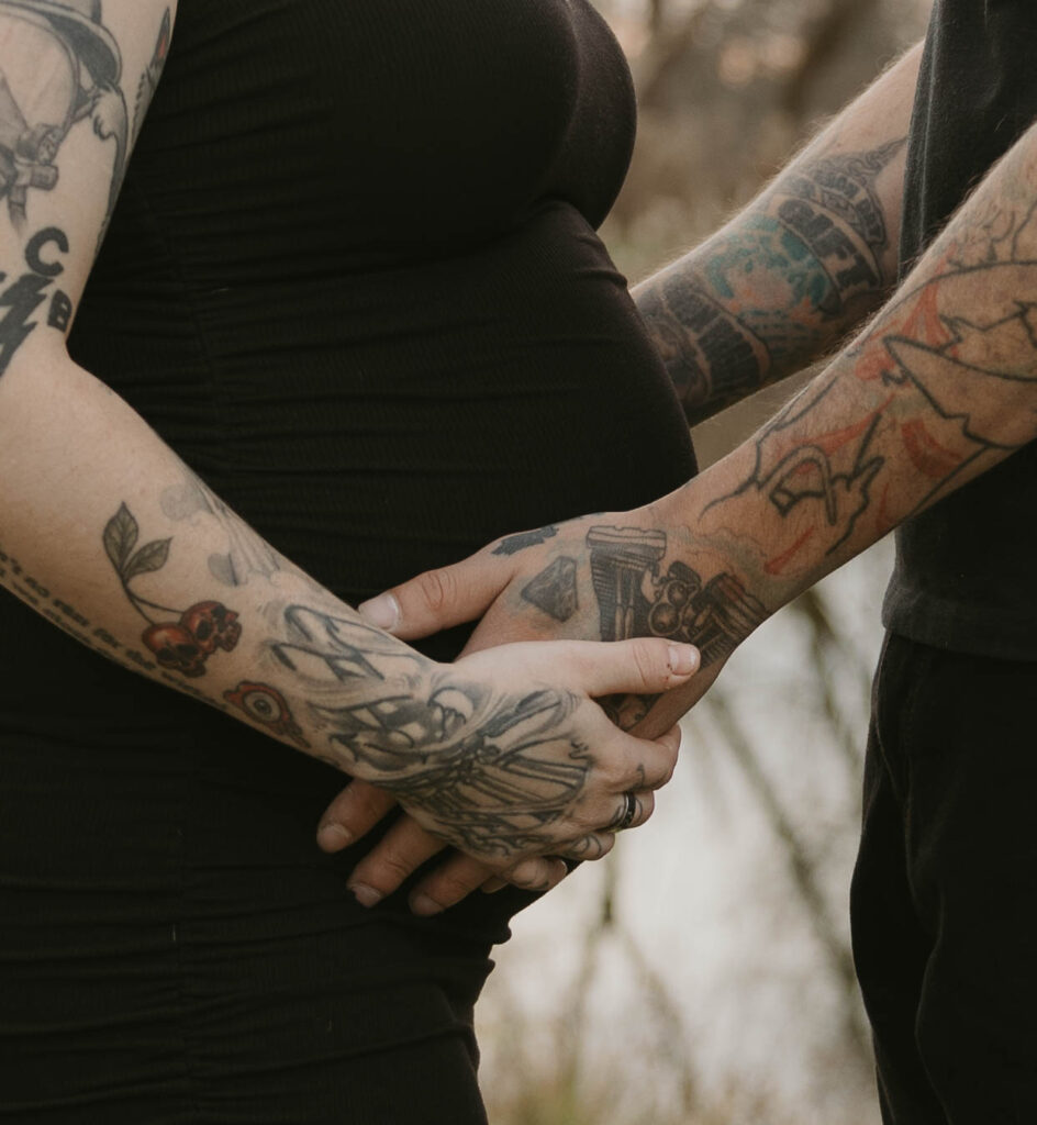 A closeup shot of a soon-to-be dad holding the belly of his partner, while she holds his hands.
