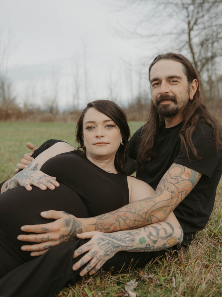 A maternity photo in a field where both parents embrace the growing belly of their first child.